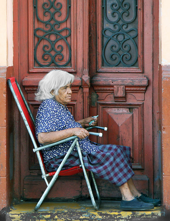 This old woman  spends the day by her door watching the passing parade.